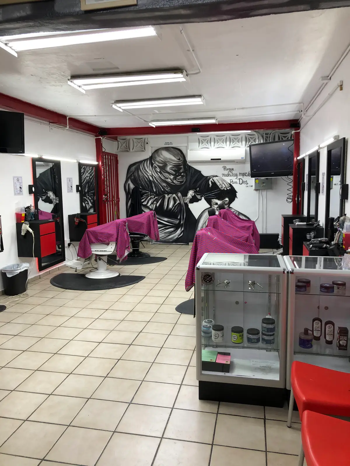 Estaciones de la barbería con capas puestas en las sillas y el mural de un barbero al fondo.