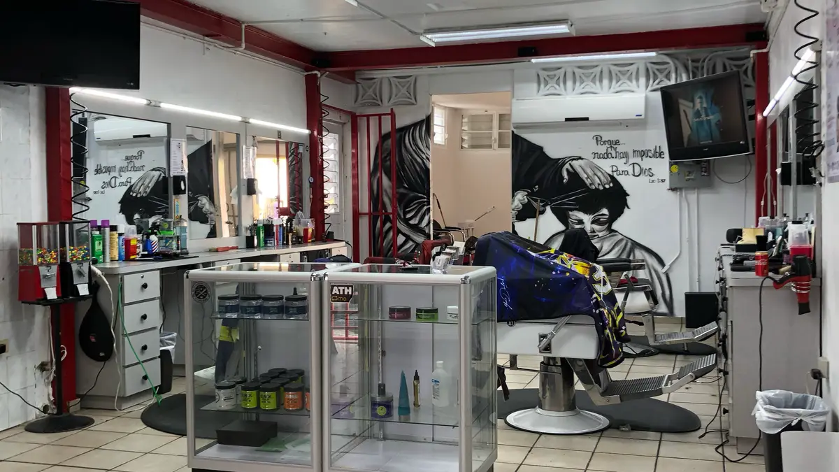 Interior de Bello Monte Hair Style: sillas de barbero, espejos, vitrinas de productos y un mural en la pared.