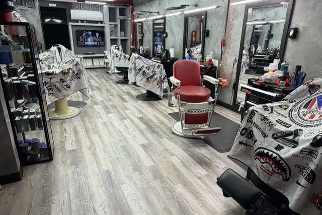 Interior renovado con piso de madera, sillas de barbero rojas y blancas, espejos y televisores.